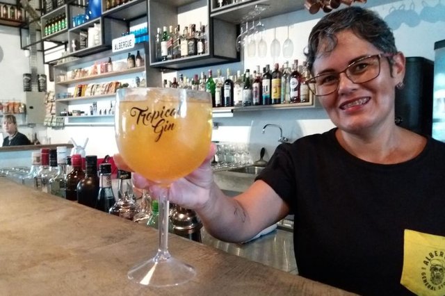 Da cor do solNos bares e restaurantes mais tops do país, de norte a sul, ele vem sendo apontado como o queridinho do verão. Eu estou falando do drink Tropical Gin, que também já deu as caras na joinvilândia. Em alguns lugares, chegam a ser pedidos por noite, 25, 35 e até 50 desses drinks. E pelo jeito é só o começo, já que a bebida tem uma mistura que combina com a estação mais quente do ano. Para dar aquela mãozinha para você, eu fui ver de perto como se faz a bebida. Segundo a bartender Josene Rodrigues Carvalho, do Albergue General Store que fica no bairro América, a receita não tem grandes segredos. É só misturar numa taça grande gin e red bull tropical mais gelo. E pronto. Você está conectado com o verão que vem ai. Da cor do solNos bares e restaurantes mais tops do país, de norte a sul, ele vem sendo apontado como o queridinho do verão. Eu estou falando do drink Tropical Gin, que também já deu as caras na joinvilândia. Em alguns lugares, chegam a ser pedidos por noite, 25, 35 e até 50 desses drinks. E pelo jeito é só o começo, já que a bebida tem uma mistura que combina com a estação mais quente do ano. Para dar aquela mãozinha para você, eu fui ver de perto como se faz a bebida. Segundo a bartender Josene Rodrigues Carvalho, do Albergue General Store que fica no bairro América, a receita não tem grandes segredos. É só misturar numa taça grande gin e red bull tropical mais gelo. E pronto. Você está conectado com o verão que vem ai.