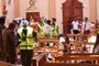 EDITORS NOTE: Graphic content / Sri Lankan security personnel walk past debris next to a dead body slumped over a bench following an explosion in St Sebastians Church in Negombo, north of the capital Colombo, on April 21, 2019. - A series of eight devastating bomb blasts ripped through high-end hotels and churches holding Easter services in Sri Lanka on April 21, killing nearly 160 people, including dozens of foreigners. (Photo by STR / AFP) / GRAPHIC CONTENT