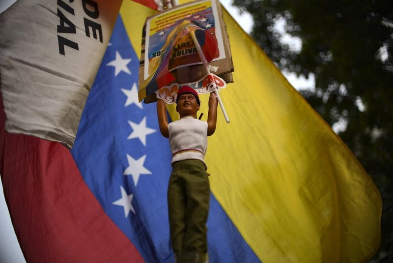 A supporters of the Venezuelas President Nicolas Maduro and who stays on a vigil in fornt of the Presidential Palace of Miraflores rises a doll representing Venezuelas late President Hugo Chavez and the national flag in Caracas, Venezuela on May 1, 2019. - Demonstrators clashed with police on the streets of the Venezuelan capital Tuesday, spurred by opposition leader Juan Guaidos call on the military to rise up against President Nicolas Maduro -- who said he had defeated an attempted coup. (Photo by YURI CORTEZ / AFP)