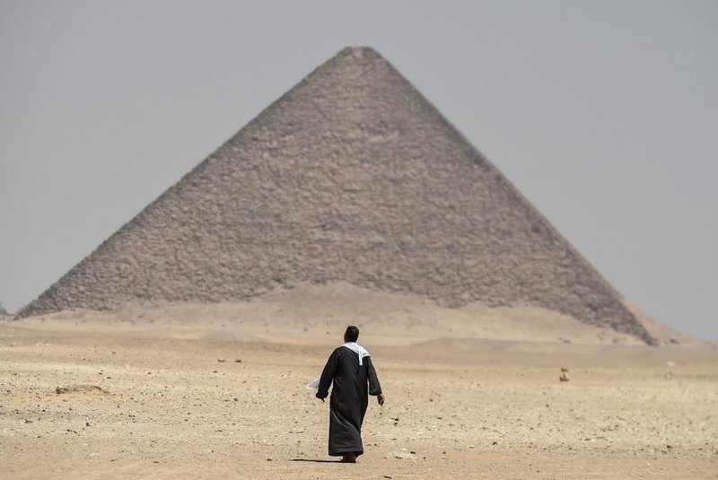 A man walks next to the Red Pyramid, in Dahshur, some 30 kilometres (20 miles) south of Cairo, on July 13, 2019. - Egyptian archaeologists unveiled Saturday several sarcophagi with some containing well-preserved mummies, along with the remains of an ancient wall dating to the Middle Kingdom nearly 4,000 years ago. The finds were made during excavation work in the ancient royal necropolis of Dahshur on the west bank of the Nile River, south of Cairo. The area is home to some of Egypts oldest pyramids including the bent pyramid of King Sneferu, the first pharaoh of Egypts 4th dynasty. (Photo by Mohamed el-Shahed / AFP)