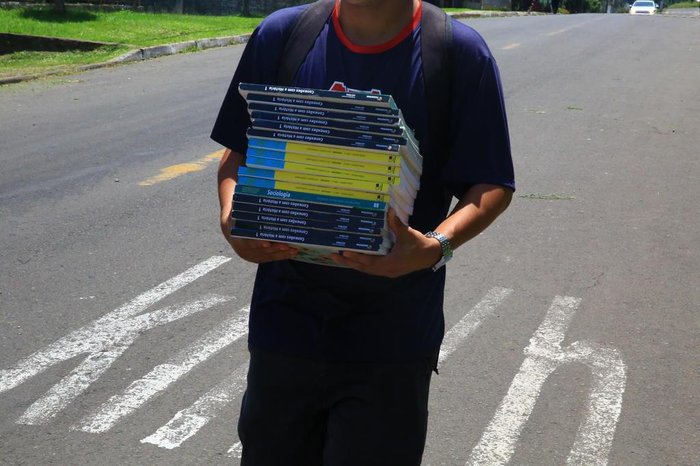 Alunos carregam livros pela rua no trajeto entre escola e CTG