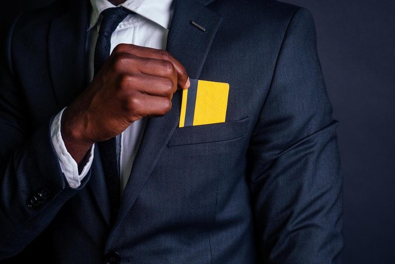  young successful businessman man in a stylish black classic suit and in cool glasses holding a yellow plastic credit card in the studio on a dark background. shopping conceptIndexador: yurakrasil.ruFonte: 223509927<!-- NICAID(14408682) -->