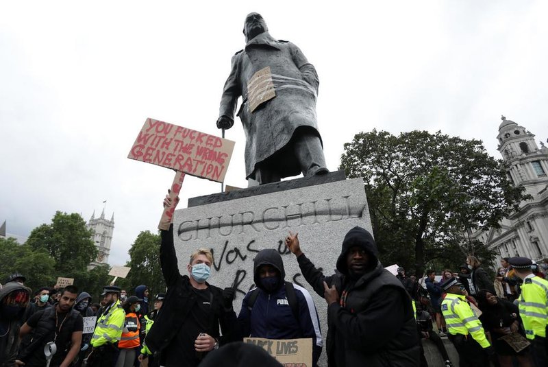 Protesters pose for a photograph in front of the defaced statue of former British prime minister Winston Churchill, with the words (Churchill) was a racist written on its base in Parliament Square, central London after a demonstration outside the US Embassy, on June 7, 2020, organised to show solidarity with the Black Lives Matter movement in the wake of the killing of George Floyd, an unarmed black man who died after a police officer knelt on his neck in Minneapolis. - Taking a knee, banging drums and ignoring social distancing measures, outraged protesters from Sydney to London on Saturday kicked off a weekend of global rallies against racism and police brutality. (Photo by ISABEL INFANTES / AFP)<!-- NICAID(14517461) -->