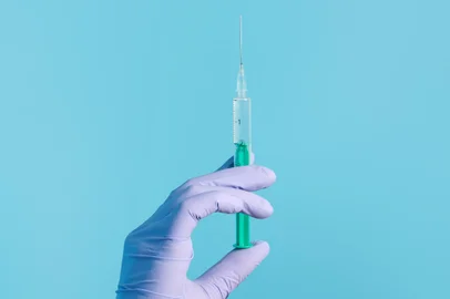 Syringe for injection in hand, latex medical gloves on hand. On a blue background.Seringa, luva, injeção, mão. Foto:  Snejana / stock.adobe.comFonte: 408254657<!-- NICAID(14840403) -->