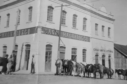 Fundada em 1915, a Casa Magnabosco confunde-se com a história de Caxias do Sul e da imigração italiana na região. Ponto de referência do Centro, ícone arquitetônico, com sua fachada minuciosamente revitalizada; e um dos nomes mais lembrados pelos consumidores quando se fala em lojas de departamentos tradicionais, o Magnabosco surgiu inicialmente como um secos & molhados, em um antigo casarão de madeira na esquina das ruas Sinimbu e Dr. Montaury.O que nem todos sabem - ou lembram - é que entre a demolição da pioneira casa em estilo colonial e a conclusão do majestoso prédio de alvenaria, em meados de 1939, o estabelecimento fundado por Raymundo Magnabosco funcionou temporariamente no edifício de dois pavimentos da esquina em frente (foto acima), pertencente à família de Giovanni Battista Serafini - pai de Flora Serafini, esposa de Raymundo.O tempo exato em que a loja ficou ali é uma incógnita, mas calcula-se que foram pelo menos três anos - em fotos da Festa da Uva de 1937 é possível ver a construção do edifício atual e a identificação “Casa Magnabosco” no sobrado dos Serafini. Já quando ficou pronto, em 1939, o moderno prédio em estilo art déco ou a abrigar a casa comercial no térreo, o Fórum e a residência do juiz no segundo andar, e o lar do proprietário no terceiro piso. Era onde Raymundo e Flora conviviam com os 12 filhos: Lucy, Girólamo, Dirceu, Zila, Otávio, Thereza Luiza, José Carlos, Ada, Nelly, Maria de Lourdes, Flora (Lola) e Hélio Antonio (falecido em 1945). Na foto: A Casa Magnabosco por volta de 1937/1938, quando funcionou no prédio da família Serafini, na esquina em frente.<!-- NICAID(15978760) -->