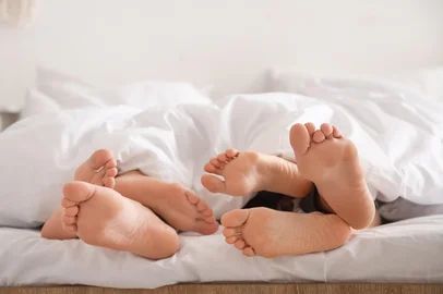 Feet of young man with two women lying under blanket in bedroom, closeup. Polyamory concept<!-- NICAID(16097428) -->