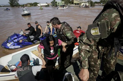 RS, Brasil, 06-05-2024: Carina Chaves (C), 35 anos, resgatada com o marido Cassiano, 41, e a filha deles, Rhadassa, 10. Equipe de militares em uma embarcacao portada Birdon, como um rebocador, com capacidade para transportar em seguranca ate 20 pessoas, traz pessoas resgatadas do bairro Chacara, em Eldorado do Sul, para estrutura de apoio na Usina do Gasometro, na orla de Porto Alegre. Foto: Mateus Bruxel / Agencia RBSIndexador: MATEUS BRUXEL<!-- NICAID(15756848) -->