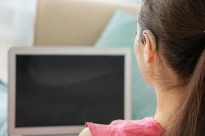 Young woman with hearing aid using laptop indoorsFonte: 191878480<!-- NICAID(15323933) -->