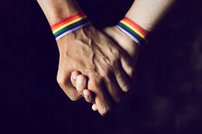 men holding hands with rainbow-patterned wristbandCasal de mãos dadas, pulseira, arco iris, LGBT. Foto: nito / stock.adobe.comFonte: 209714746<!-- NICAID(15163650) -->