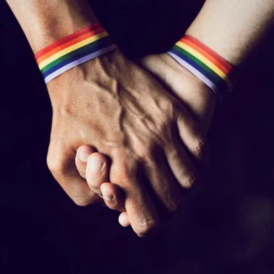 men holding hands with rainbow-patterned wristbandCasal de mãos dadas, pulseira, arco iris, LGBT. Foto: nito / stock.adobe.comFonte: 209714746<!-- NICAID(15163650) -->