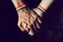 men holding hands with rainbow-patterned wristbandCasal de mãos dadas, pulseira, arco iris, LGBT. Foto: nito / stock.adobe.comFonte: 209714746<!-- NICAID(15163650) -->