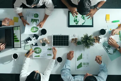 Top down view of business team discussing about using clean energy and sustainable investment at meeting table with wind mill, document with environmental graph and wooden house model. Alimentation.<!-- NICAID(16169305) -->