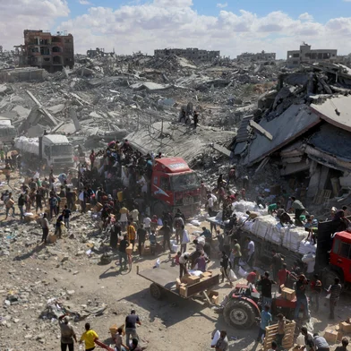 Palestinians rally around aid trucks which entered from the Karem Abu Salem crossing, in Khan Yunis in the southern Gaza Strip on October 12, 2025, as a ceasefire between Israel and Palestinian factions holds in the besieged territory. A Gaza ceasefire was holding for a third day on October 12, ahead of a US-proposed hostage-prisoner exchange and a summit aimed at charting a path to peace after two years of war. (Photo by Omar AL-QATTAA / AFP)Editoria: WARLocal: Khan YunisIndexador: OMAR AL-QATTAASecao: refugeeFonte: AFPFotógrafo: STR<!-- NICAID(16144487) -->
