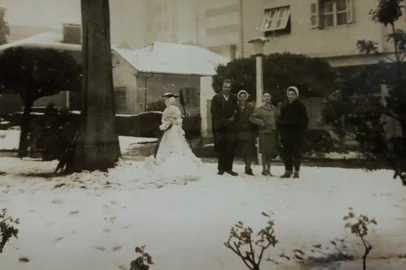Neve na Praça da Bandeira em 1965. Fenômeno ocorreu em 19 e 20 de agosto de 1965 e atraiu moradores do bairro São Pelegrino, como o casal Mirlene Dal Pos Rossi e Raul Rossi. Na foto, a partir da esquerda, Raul Rossi, Mirlene Dal Pos Rossi, Vilma Zini e Lorita Rech. Texto da matéria:A antiga Praça Rui Barbosa (Dante Alighieri) foi o cenário eternizado em milhares de fotos captadas em 19 e 20 de agosto de 1965, quando Caxias e dezenas de cidades da Serra ficaram cobertas de branco. Mas, a poucos metros dali, outro cenário também chamou a atenção: a Praça da Bandeira.Foi para lá que moradores do bairro São Pelegrino e funcionários da antiga Importadora Comercial se dirigiram quando a neve começou a acumular. Parte dessa história foi recordada pela leitora Mirlene Dal Pos Rossi, 82 anos, que à época residia com a família na Rua Feijó Jr., quase na esquina com a Dezoito, a duas quadras dali. São do acervo de dona Mirlene as imagens reproduzidas nesta página, em que ela aparece junto do então futuro marido Raul Rossi e das irmãs Vilma Zini e Lorita Rech, todas funcionárias da Importadora na época.<!-- NICAID(15453696) -->