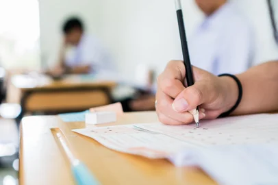 High school university student holding pencil writing exam on paper answer sheet, writing examination room doing final test in classroom with thai uniform. Education assessment ConceptFonte: 285660586<!-- NICAID(14793465) -->