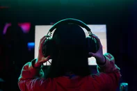 Teenage Girl Gamer Wearing Headphones Playing Video Game on ComputerTeenage girl with long dark hair wearing headphones sitting in front of computer monitor gaming in dimly lit roomFonte: 1564394264<!-- NICAID(16165016) -->