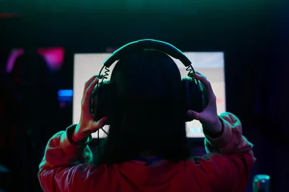 Teenage Girl Gamer Wearing Headphones Playing Video Game on ComputerTeenage girl with long dark hair wearing headphones sitting in front of computer monitor gaming in dimly lit roomFonte: 1564394264<!-- NICAID(16165016) -->