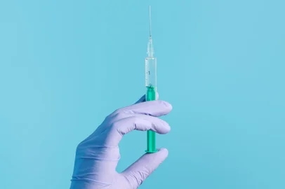Syringe for injection in hand, latex medical gloves on hand. On a blue background.Seringa, luva, injeção, mão. Foto:  Snejana / stock.adobe.comFonte: 408254657<!-- NICAID(14840403) -->
