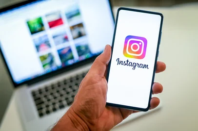Close up view of hand with smartphone and Instagram logo on display. Laptop on background. New technology, social media,  network, communication,  concept. Milan, Italy - October 2021<!-- NICAID(15869163) -->