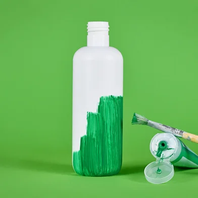 Greenwashing concept with white plastic bottle being painted green<!-- NICAID(16015190) -->