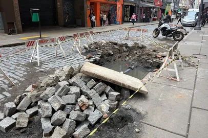 Maria Ferreira / Rádio Gaúcha PORTO ALEGRE (15/10/2026) - Uma obra do Departamento Municipal de Água e Esgotos (Dmae) na Rua dos Andradas, próximo à esquina com a Rua Doutor Flores, no Centro Histórico de Porto Alegre, tem causado transtornos a pedestres e comerciantes da região. A intervenção está em andamento desde junho e mantém um buraco aberto na via. Segundo o departamento, os trabalhos na rede de drenagem devem ser concluídos nesta sexta-feira (16). Foto de Maria Ferreira/Rádio Gaúcha.<!-- NICAID(16388011) -->