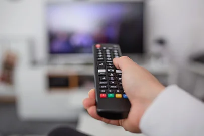 Watching TV and using remote controller. Hand with remote controller changing channels or opening apps on smart tvWatching TV and using remote controller. Hand with remote controller changing channels or opening apps on smart tvFonte: 310675434<!-- NICAID(16000348) -->