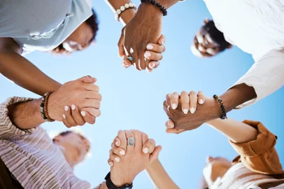 Diversity, support and people holding hands in trust and unity for community against sky background. Hand of diverse group in solidarity for united team building collaboration and teamwork success.<!-- NICAID(15909361) -->