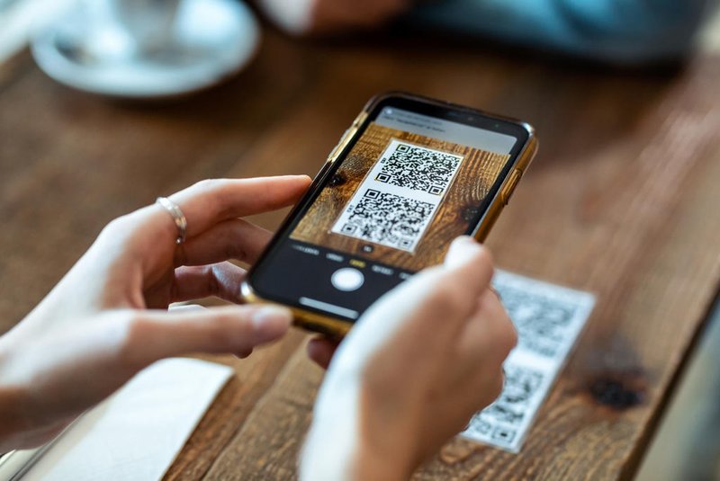 Close up of young woman hands using the smart phone to scan the qr code to select food menu in the restaurant. <!-- NICAID(15483261) -->