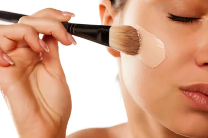 A young woman applied liquid foundation on her face with a brushFonte: 135109423<!-- NICAID(15886739) -->