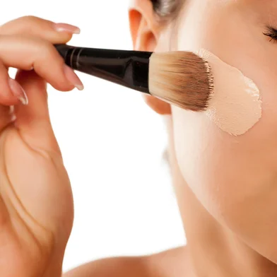 A young woman applied liquid foundation on her face with a brushFonte: 135109423<!-- NICAID(15886739) -->