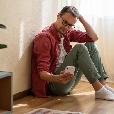 Upset young man holding smartphone waiting for ex-girlfriend call while sitting on floor at homeHomem esperando mensagem - Foto: DimaBerlin/stock.adobe.comFonte: 545688027<!-- NICAID(15743264) -->