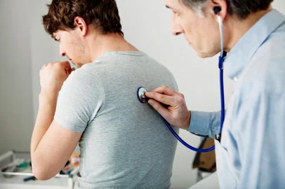Imagem que ilustra um médico pneumologista examinando um paciente que está tossindo<!-- NICAID(15420800) -->