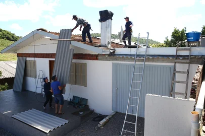Porthus Junior / Agencia RBS FLORES DA CUNHA, RS, BRASIL, 11/12/2025. Após a passagem de um tornado, na noite de segunda-feira (08/12), moradores da localidade de Travessão Alfredo Chaves, no interior de Flores da Cunha, trabalham nas obras de reconstrução e limpeza. Na foto, estragos na residência de Eni Stuani Wrensinski, 67 (embaixo à E), na rua dos Imigrantes. Os voluntários Claudimir Kremer (no telhado à D), 48 e José Antônio de Farias, 65, ajudam na reconstrução. (Porthus Junior/Agência RBS)<!-- NICAID(16184961) -->