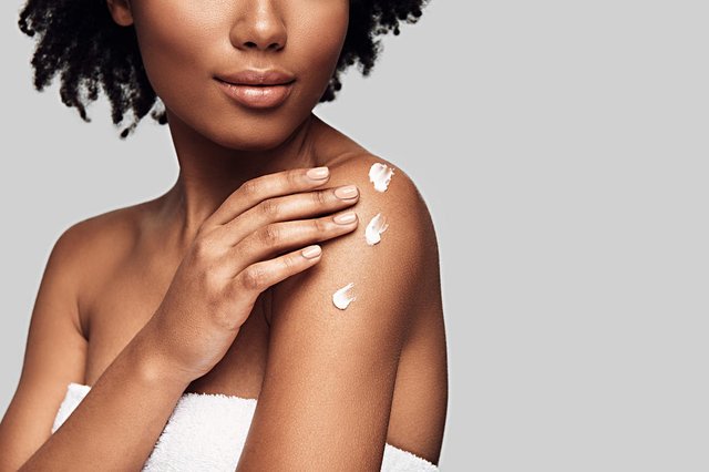 Beauty routine. Close up of young African woman applying body cream and smiling while standing against grey backgroundIndexador:                                 Fonte: 237545816<!-- NICAID(14646768) -->