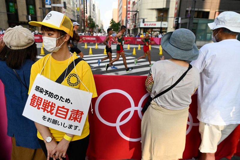 A volunteer wearing a sign reading "Don't stop to watch the race due to the coronavirus disease restrictions" stands by people gathered to watch the men's 20km race walk final during the Tokyo 2020 Olympic Games at the Sapporo Odori Park in Sapporo on August 5, 2021. (Photo by Charly TRIBALLEAU / AFP)<!-- NICAID(14856364) -->