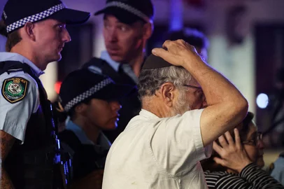 DAVID GRAY / AFP A member of the Jewish community reacts as he walks with police towards the scene of a shooting at Bondi Beach in Sydney on December 14, 2025. Australian police said two people were in custody following reports of multiple gunshots on December 14 at Sydney's famed Bondi Beach, urging the public to take shelter. (Photo by DAVID GRAY / AFP)<!-- NICAID(16186380) -->
