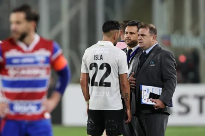 Colo-Colo's defender #22 Mauricio Isla (C) talks to a CONMEBOL official after fans of Colo Colo enter the pitch during the Copa Libertadores group stage football match between Chile's Colo Colo and Brazil's Fortaleza at the Monumental David Arellano stadium in Santiago, on April 10, 2025. Two people were killed Thursday in a stampede as a group of fans tried to force their way into Colo Colo's Monumental stadium in Santiago to watch the match against Brazil's Fortaleza for the Copa Libertadores 2025, authorities said. (Photo by Javier TORRES / AFP)<!-- NICAID(16014888) -->