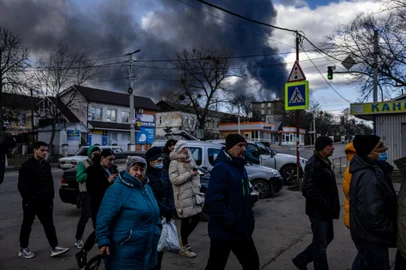 People stand in line in front of a supermarket while smoke billows over the town of Vasylkiv just outside Kyiv on February 27, 2022, after overnight Russian strikes hit an oil depot. - Ukraine's foreign minister said on February 27, that Kyiv would not buckle at talks with Russia over its invasion, accusing President Vladimir Putin of seeking to increase "pressure" by ordering his nuclear forces on high alert. (Photo by Dimitar DILKOFF / AFP)<!-- NICAID(15028751) -->