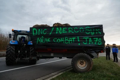 Members of Young Farmers of the Yvelines (JA - Jeunes Agriculteurs des Yvelines) position a tractor with a sign which reads "DNC / Mercosur, same battle" to partially blocade the N12 road in Mere in the Yvelines outside Paris on December 16, 2025, as part of nationwide action by farmers to protest against the government's mandatory culling protocol for cattle herds affected by lumpy skin disease (dermatose nodulaire contagieuse), a viral disease first detected in France in June 2025 that has led to the slaughter of over 3,000 cattle across more than 110 outbreaks nationwide, and against an EU trade deal with Mercosur countries. (Photo by GEOFFROY VAN DER HASSELT / AFP)<!-- NICAID(16187544) -->