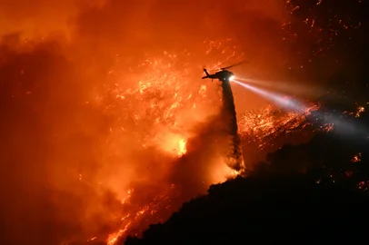 A fire fighting helicopter drops water as the Palisades fire grows near the Mandeville Canyon neighborhood and Encino, California, on January 11, 2025. The Palisades Fire, the largest of the Los Angeles fires, spread toward previously untouched neighborhoods January 11, forcing new evacuations and dimming hopes that the disaster was coming under control. Across the city, at least 11 people have died as multiple fires have ripped through residential areas since January 7, razing thousands of homes in destruction that US President Joe Biden likened to a "war scene." (Photo by Patrick T. Fallon / AFP)<!-- NICAID(15952298) -->