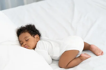black african american baby sleeping on a white mattress.Fonte: 440423807<!-- NICAID(15565313) -->