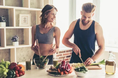 Beautiful young sports people are talking and smiling while cooking healthy food in kitchen at homeFonte: 144333550<!-- NICAID(15744717) -->