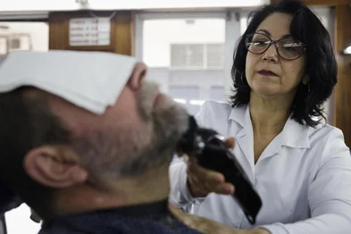 PORTO ALEGRE, RS, BRASIL, 19-08-2025: A barbeira Marta Ribeiro Soares atende a um cliente no Salão Fígaro. Ela é a única mulher a ocupar uma das seis cadeiras do  ponto tradicional do centro histórico de Porto Alegre. Foto: Mateus Bruxel/Agência RBSIndexador: MATEUS BRUXEL<!-- NICAID(16104984) -->
