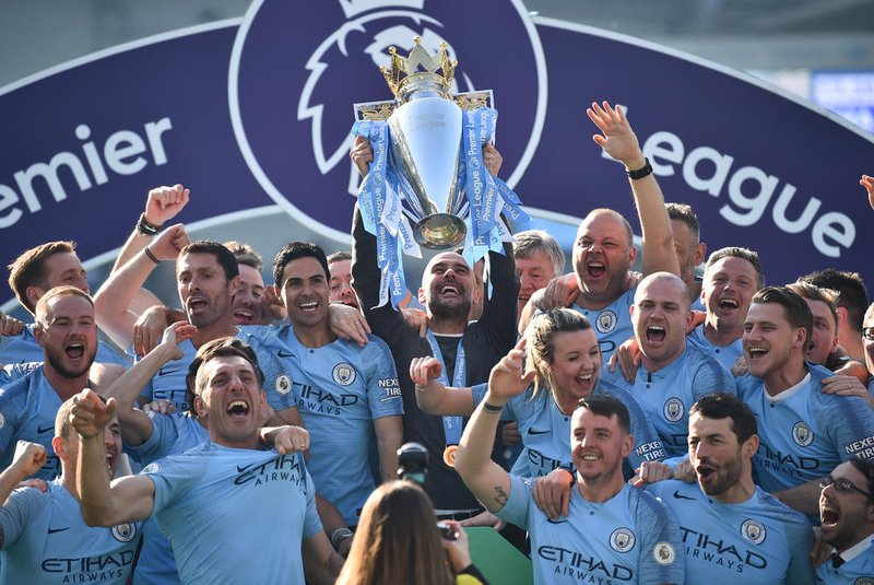 Manchester City's Spanish manager Pep Guardiola (C) lifts the Premier League trophy with staff members after their 4-1 victory in the English Premier League football match between Brighton and Hove Albion and Manchester City at the American Express Community Stadium in Brighton, southern England on May 12, 2019. - Manchester City held off a titanic challenge from Liverpool to become the first side in a decade to retain the Premier League on Sunday by coming from behind to beat Brighton 4-1 on Sunday. (Photo by Glyn KIRK / AFP) / RESTRICTED TO EDITORIAL USE. No use with unauthorized audio, video, data, fixture lists, club/league logos or 'live' services. Online in-match use limited to 120 images. An additional 40 images may be used in extra time. No video emulation. Social media in-match use limited to 120 images. An additional 40 images may be used in extra time. No use in betting publications, games or single club/league/player publications. / Editoria: SPOLocal: BrightonIndexador: GLYN KIRKSecao: soccerFonte: AFPFotógrafo: STR<!-- NICAID(14075023) -->