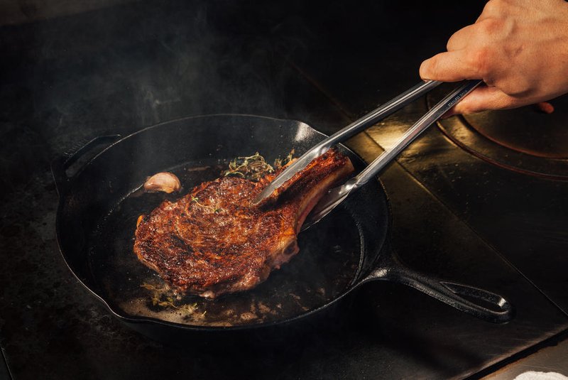 Cooking steak in a cast iron pan in a fine dining restaurant.Indexador: Troyce HoffmanFonte: 206541816Fotógrafo: Photographer<!-- NICAID(15705572) -->