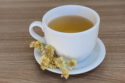 A cup of hot tea made with Macela flowers (Achyrocline satureioides), and Macela flowers on the side, on a wooden background. Macela flowers, medicinal plant, natural, in Brazil.Fonte: 496731868<!-- NICAID(15577823) -->