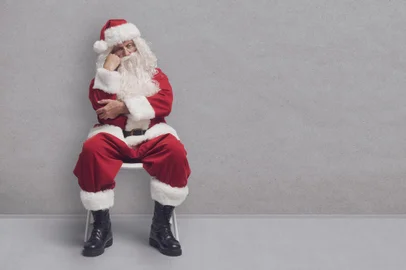 Bored Santa Claus sitting on a chair and waiting for a job interviewFonte: 537234602<!-- NICAID(15629824) -->