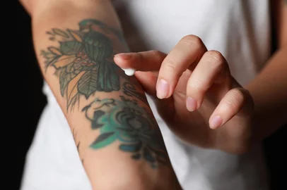 Woman applying cream on her arm with tattoos against black background, closeupIndexador: Olga Yastremska, New Africa, AfrFonte: 480220127<!-- NICAID(15179574) -->