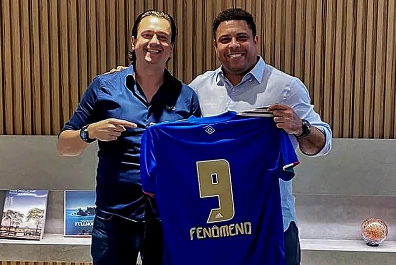 Handout picture released by the Cruzeiro Esporte football club showing its president Sergio Santos Rodrigues (L) and Brazilian former striker Ronaldo (R) posing for a picture holding a Cruzeiro jersey, during a meeting in Sao Paulo, Brazil, on December 18, 2021. - Former Brazilian striker Ronaldo announced on Saturday that he would buy Cruzeiro, a club where he made his professional debut at the age of 16, but which has languished in the second division for two seasons. (Photo by Cruzeiro Football Club / AFP) / RESTRICTED TO EDITORIAL USE - MANDATORY CREDIT AFP PHOTO / CRUZEIRO FOOTBALL CLUB - NO MARKETING NO ADVERTISING CAMPAIGNS -DISTRIBUTED AS A SERVICE TO CLIENTSEditoria: SPOLocal: Sao PauloIndexador: -Secao: soccerFonte: Cruzeiro Football ClubFotógrafo: Handout<!-- NICAID(14972117) -->