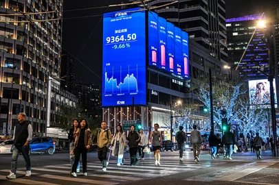 People walk next to a screen with a stocks indicator in the Jing'an district in Shanghai on April 7, 2025. Asian equities collapsed on a black Monday on April 7 for markets after China hammered the United States with its own hefty tariffs, ramping up a trade war many fear could spark a recession. (Photo by Hector RETAMAL / AFP)<!-- NICAID(16012213) -->